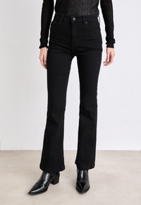 Svart høy midje jeans med flared ben, med en jevn denim tekstur, subtile sømdetaljer og en rå kant. Kombinert med svarte spisse ankelstøvler.