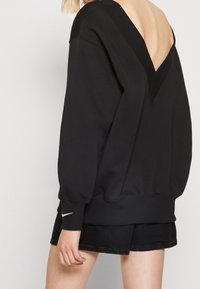 Zwarte sweatshirt met een diepe V-hals en geribbelde accenten, voorzien van volumineuze mouwen en een relaxte pasvorm, gecombineerd met zwarte shorts.