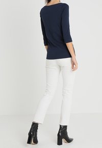 Marinblå topp med trekvartslång ärm som matchas med vita skinny jeans och svarta högklackade ankelstövlar. Toppen har en vid halsringning och en figurnära design.