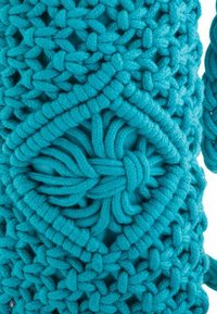 Turquoise macramé bag with a textured design, featuring woven patterns, a knot detail at the center, and braided straps.