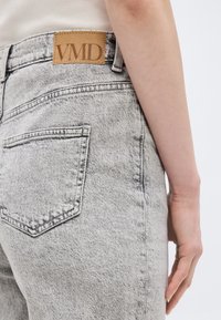 Κοντινή λήψη ενός ατόμου που φοράει ανοιχτό γκρι τζιν με πλύσιμο, με πίσω τσέπη και καφέ δερμάτινη ετικέτα με την επιγραφή "VMD".