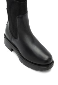 Stivale alla caviglia in pelle nera con gambale in tessuto rigato, punta rotonda e suola spessa, caratterizzato da una texture liscia e un design minimalista.