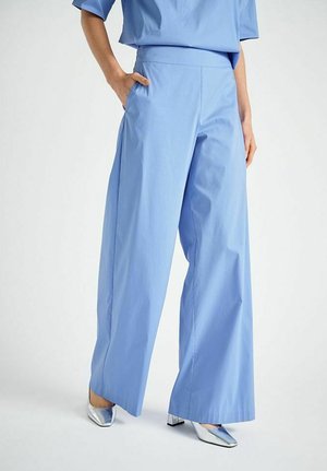 Pantalon large bleu clair porté avec un haut assorti et des chaussures à talon bloc argentées à bout carré sur un fond uni.