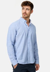Chemise bleu clair à boutons avec un motif texturé, manches longues et col doux. Détail notable : doublure de col intérieure contrastante.