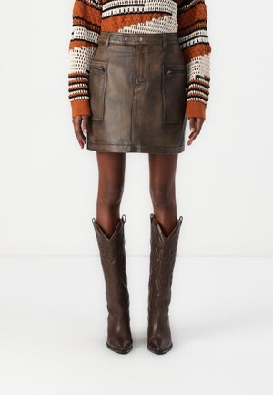 Brun skinnminiskjørt med glidelåslommer foran, brukt med brune cowboy støvler med spiss tå og preget design.