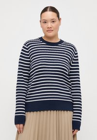 Navy blue sweater with white horizontal stripes, ribbed texture, round neck, and long sleeves, paired with a pleated beige skirt.