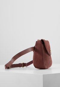 Torba na ramię wykonana z bordowej zamszowej tkaniny o płaskim, zaokrąglonym kształcie. Posiada klapę z złotym guzikiem i brązowym skórzanym paskiem.