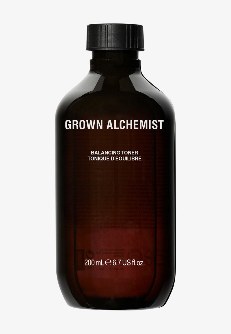 Bursztynowa szklana butelka z czarną nakrętką, opisana jako "GROWN ALCHEMIST BALANCING TONER", o pojemności 200 ml, z minimalistycznym wzorem tekstowym.