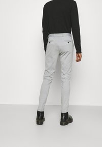 Szare, dopasowane spodnie o gładkiej fakturze, z dwoma tylnymi kieszeniami i czarnymi guzikami, zestawione z czarnym topem z długim rękawem.