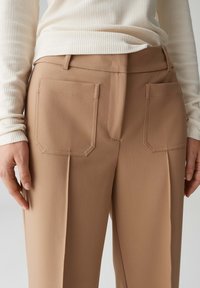 Beige op maat gemaakte broek met twee rechthoekige achterzakken, een gladde textuur en een voorpand met plooien.
