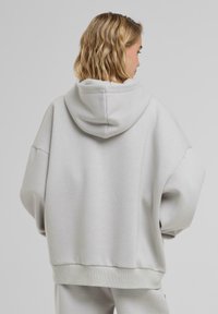 Svjetlosiva oversized kapuljača izrađena od mekanog materijala, s kapuljačom i rebrastim manžetama, te bešavnom dizajnom stražnje strane.