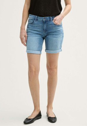 Shorts en jean bleu clair avec des revers, cinq poches et une coupe ajustée. Portés avec des ballerines noires.