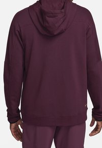 Sweat à capuche couleur bordeaux avec une texture douce, une coupe ample et des coutures contrastées. Présente un petit logo sur l'ourlet inférieur.