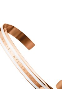 Cevljasta narukvica iz rose zlatnega kovine z belo črto. Na eni strani je vtisnjen napis "DANIEL WELLINGTON". Gladek, poliran zaključek.