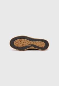 Black sneaker with a textured rubber sole. Features a wavy pattern, perforations for ventilation, and a light brown outsole for grip.