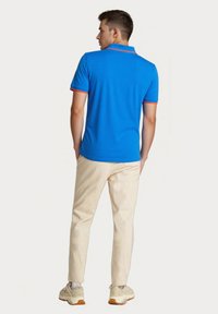 Blå polo skjorte med rød kraverand, parret med beige bukser. Skjorten har et struktureret stof, og outfittet inkluderer lyse sneakers.