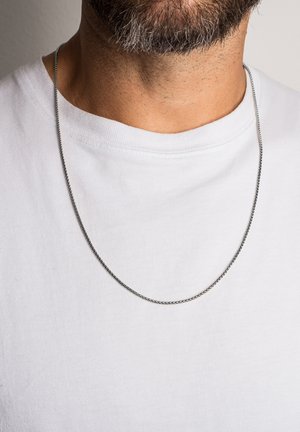Silver-toned chain necklace worn over a white crew neck t-shirt, featuring a smooth texture and thin, subtle links.