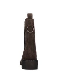Botín de ante marrón con una suela negra gruesa. Presenta una correa trasera con un detalle de anillo metálico y paneles elásticos laterales para un mejor ajuste.