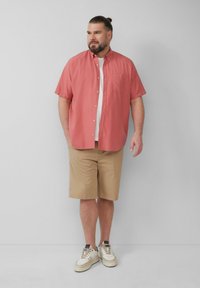 Korte mouwen koraalkleurige overhemd met knopen, beige shorts en witte sneakers. Het shirt heeft een borstzak; een gladde stof; een relaxte pasvorm.