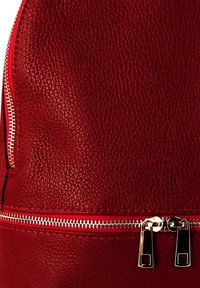 Sac à dos en cuir rouge texturé avec des zippers argentés, des coutures visibles et deux compartiments zippés. Dessus arrondi pour un design élégant.