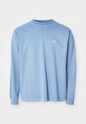 Lyseblå langærmet skjorte lavet af blødt stof, har rund hals, ribbede ærmegab og en lille hvid "obey"-logo på brystet.