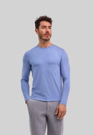 Hellblaues Langarm-T-Shirt aus weichem Stoff, mit rundem Ausschnitt und taillierter Silhouette, kombiniert mit grauen Jogginghosen.