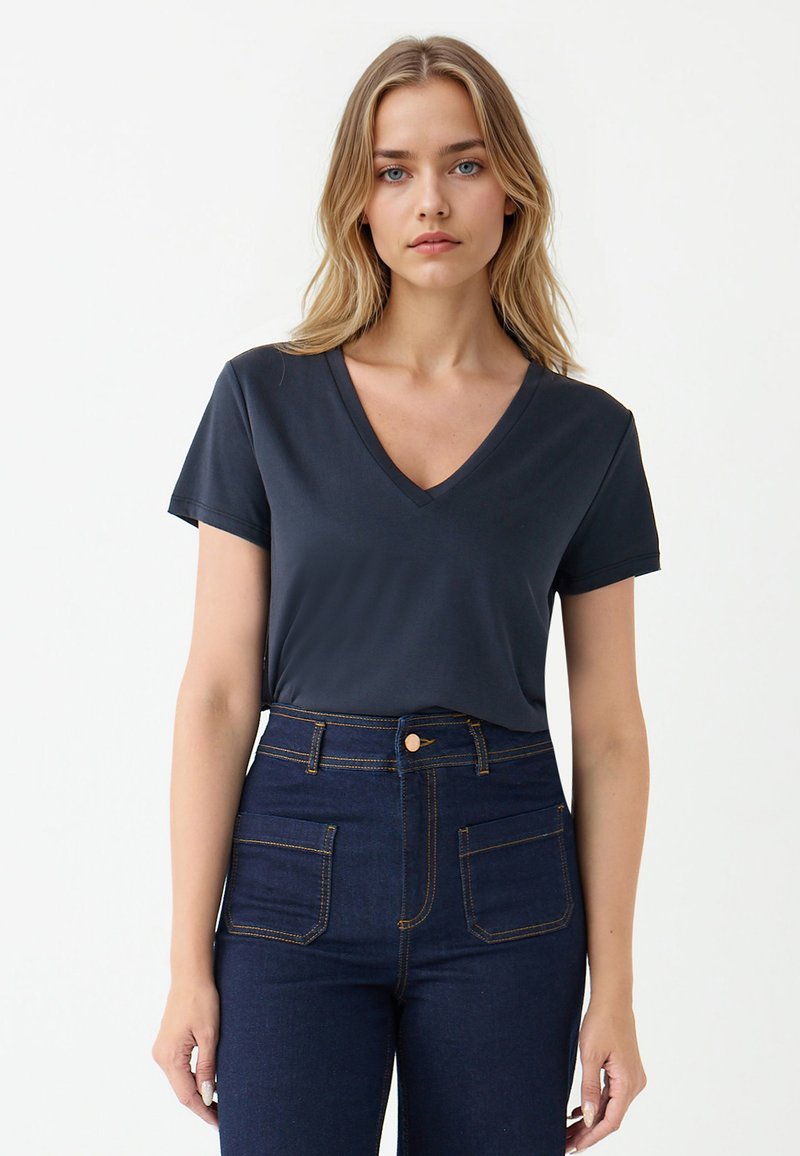 Ciemnoniebieski t-shirt z dekoltem w serek wykonany z miękkiego materiału, w połączeniu z wysokimi, ciemnoniebieskimi dżinsami z kontrastowymi szwami i dwiema przednimi kieszeniami.