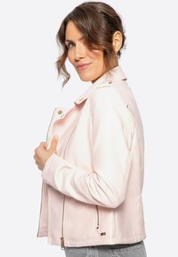 Chaqueta de piel sintética color rosa claro con un diseño ajustado, bolsillos con cremallera y hombreras. Textura suave y detalles en dorado.
