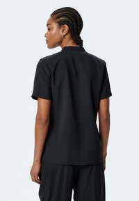 Camisa negra de manga corta con una textura suave y un cuello clásico. Presenta un diseño simple sin patrones ni adornos.