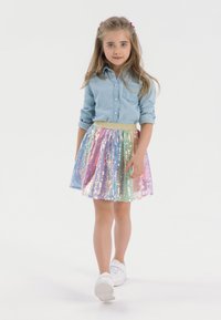 Denim-Hemd mit Knöpfen, bunte Pailletten-Rock mit goldenem Taillenbund, weiße Sneakers, heller Hintergrund, Mädchen läuft nach vorne.
