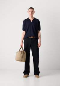 Marineblå polo, svarte bukser, beige veske med brune detaljer og brune sko. Har kort ermer og en avslappet passform.
