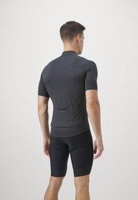 Maillot de cyclisme à manches courtes en tissu gris foncé avec une coupe ajustée. Il dispose d'une poche arrière et d'une texture lisse, associé à un short de cyclisme noir.