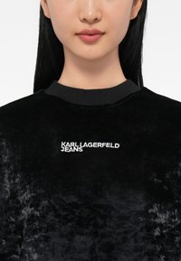 Felpa in velluto nero con scollo rotondo e logo ricamato "KARL LAGERFELD JEANS" in bianco sul lato sinistro del petto.