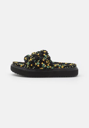 Sandalia negra tipo slide con parte superior trenzada y patrón floral amarillo en la plantilla y suela acolchadas.