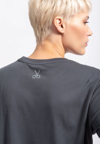 Grijze katoenen t-shirt met een subtiele scharenlogo op de achterhals. Zachte textuur met een relaxte pasvorm en eenvoudig ontwerp.