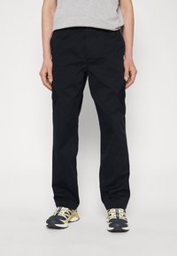 Pantalones negros ligeros con un diseño de pierna recta y bolsillos laterales, combinados con zapatillas deportivas blancas y amarillas.