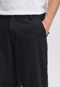 Svarte linstøvler med avslappet passform, utstyrt med glidelåsfly, knappelukking og sidelommer. Jevn tekstur og rene linjer.