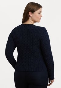 Mørkeblå kabelstrikket genser med rund halslinning og ribbestrikkede mansjetter og kant. Teksturen viser et hevet mønster gjennom hele stoffet.