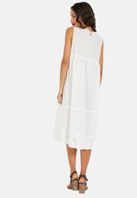 Vestido blanco sin mangas con una silueta acampanada, que presenta detalles bordados en el dobladillo y un diseño de espalda en forma de ojal.