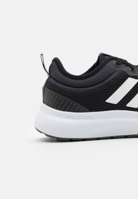 Czarny trampek z przewiewną siateczkową cholewką, białymi paskami po bokach i grubą podeszwą cloudfoam. Teksturowane akcenty zwiększają stabilność.