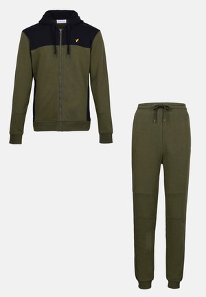 Haut de sweatshirt à zip vert olive avec une section supérieure noire et un logo jaune, associé à un pantalon ajusté coordonné avec des détails de panneaux au niveau des genoux.