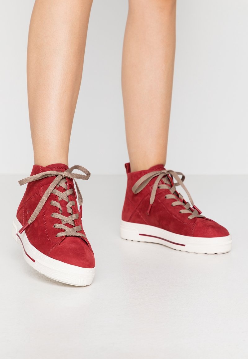 Czerwone zamszowe sneakersy za kostkę z beżowymi sznurowadłami, białą gumową podeszwą i czerwonymi akcentami. Charakteryzują się teksturowanym wykończeniem i sznurowanym fasonem.