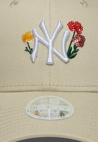 Μπεζ καπέλο μπέιζμπολ με λευκό κεντημένο λογότυπο "NY" και ανθώδη διακοσμητικά σε κόκκινο, κίτρινο και πράσινο. Διαθέτει υφή υφάσματος και κυρτή μπροστινή άκρη.