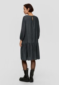 Schwarz-weiß karierter Kleid mit langen Puffärmeln, einem gerafften, gestuften Saum und einem Schlüsselloch-Rücken-Detail, kombiniert mit schwarzen kniehohen Stiefeln.