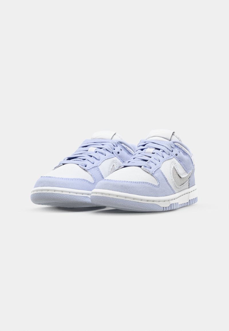 Zapatillas de deporte de color azul claro, fabricadas con materiales textiles y sintéticos, que presentan una puntera blanca, cordones blancos y un logo plateado en el lateral.