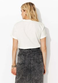 T-shirt en coton écru avec des manches retroussées, associé à une jupe en denim noire taille haute avec des poches arrière et des coutures visibles.