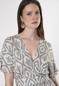 Leichtes Kleid in Pastellrosa und Grün mit geometrischem Muster. Verfügt über einen V-Ausschnitt und kurze Ärmel. Strukturierte Details an der Taille.