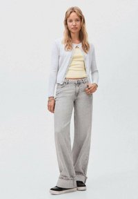 Lichtgrijze cardigan over een gele cropped top, gecombineerd met wijde grijze jeans en zwart-witte sneakers. Eenvoudig ontwerp, zachte texturen.