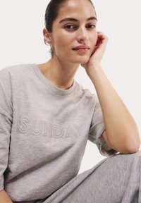 Lichtgrijze t-shirt met "SUNDAY" geborduurd in een iets donkerdere tint. Zachte stof, relaxte pasvorm en opgerolde mouwen.