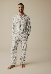 Herren-Pyjama-Set aus weißem Stoff mit schwarzem Muster von Waldlandschaften. Es verfügt über lange Ärmel, einen Kragen, eine durchgehende Knopfleiste und lockere Hose.